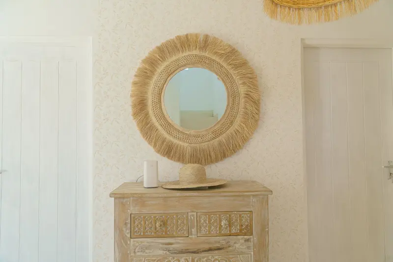 A round rattan mirror over a carved chest